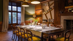 Une salle à manger avec une longue table dressée pour le repas, des chaises en bois, une bibliothèque et une cheminée.
