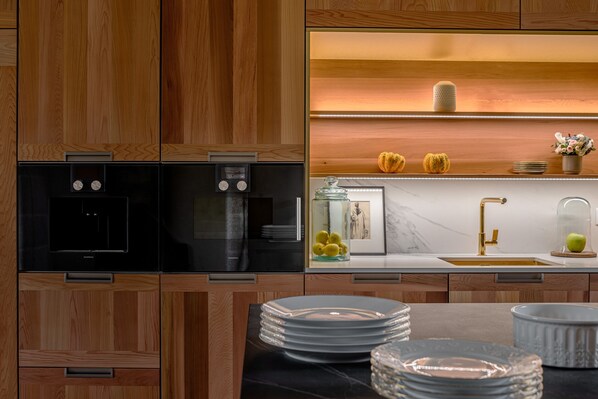 Una cocina moderna con armarios de madera, electrodomésticos negros y encimera de mármol.