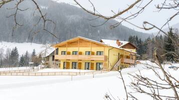 Ein großes, gelbes Gebäude mit mehreren Balkonen und einer überdachten Außenfläche, umgeben von Schnee und Bäumen.