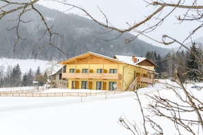 A large, yellow building with multiple balconies and a covered outdoor area, surrounded by snow and trees. - Gasthof Wachter (Gaal)