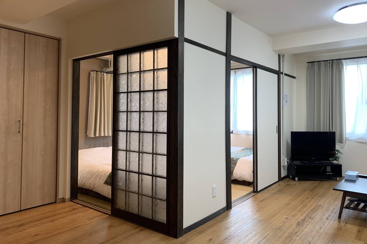 A room with a sliding shoji screen, wooden flooring, a bed, a TV, and a desk.