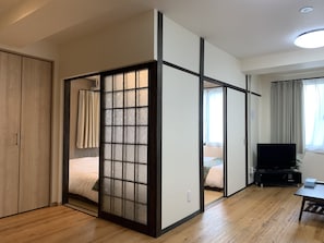 Una habitación con un fusuma corredero, suelo de madera, cama, televisor y escritorio.