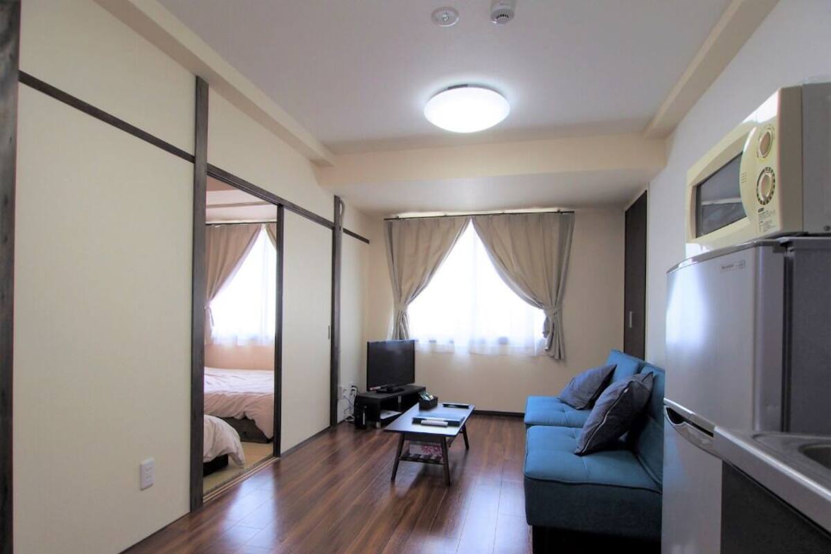 A compact living space with a sofa, a small table, a television, and a kitchenette area.