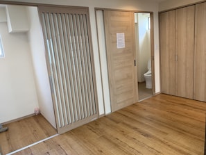 Habitación con piso de madera, puerta corredera con panel de persianas verticales, inodoro y armario.