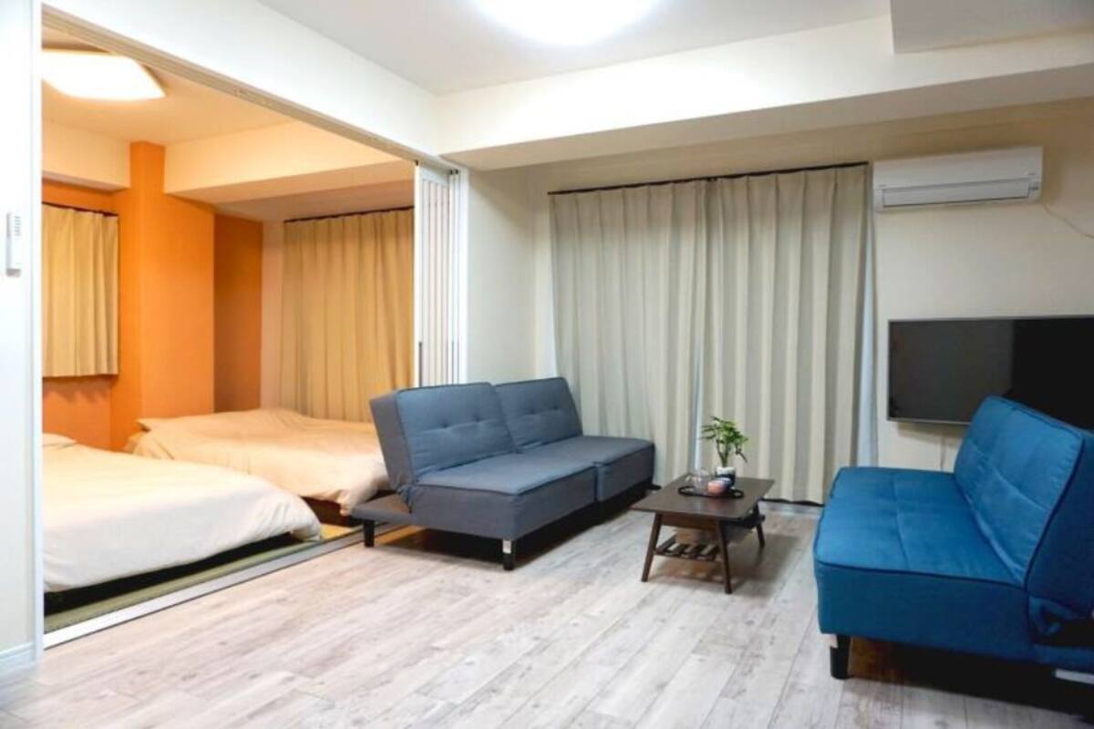 A hotel room with a sofa, a bed, a small table with a plant, and a TV on the wall.