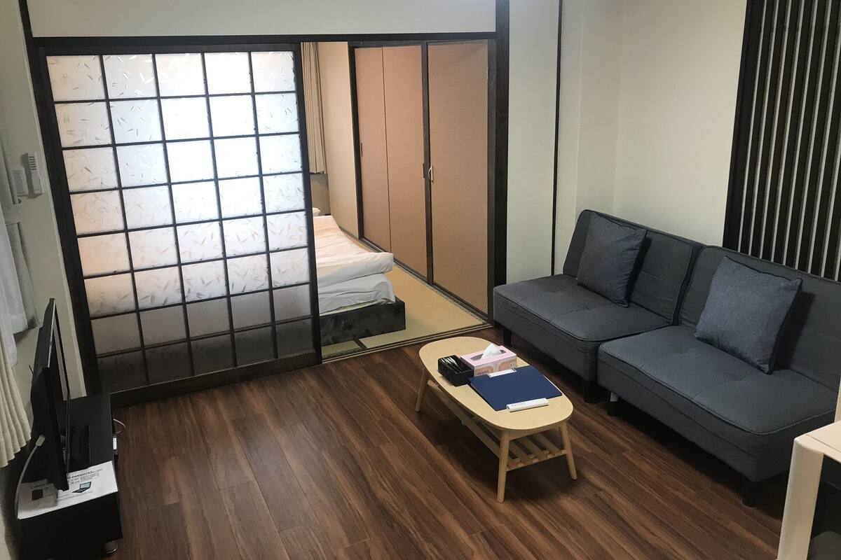 A compact living space with a futon bed, a sofa, and a small wooden table.