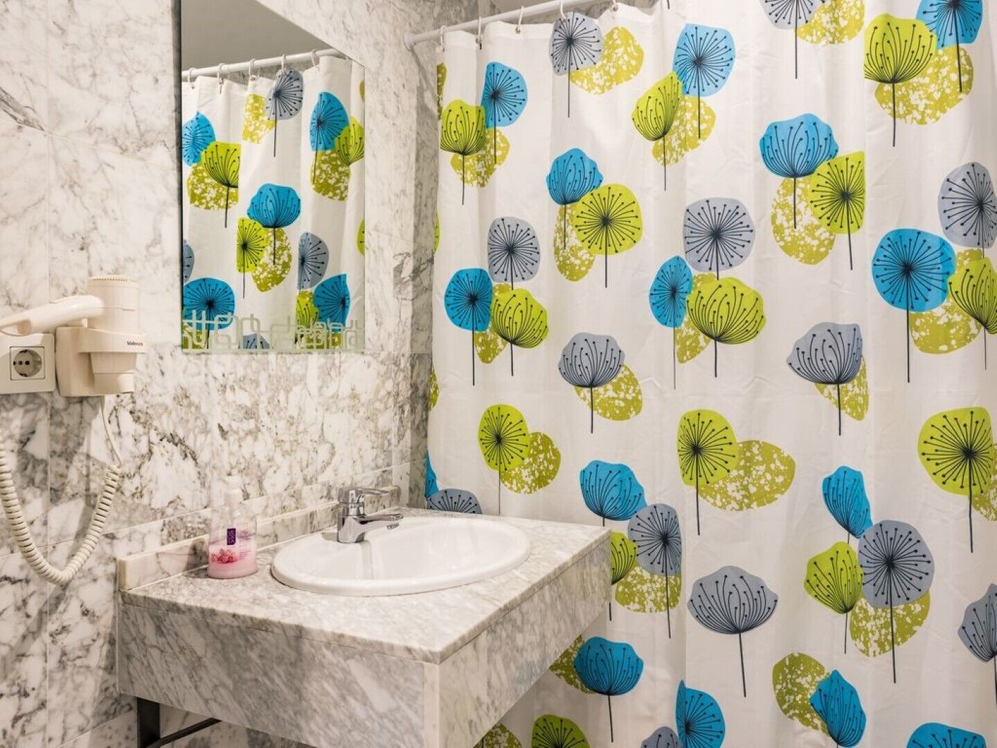 Un baño con lavamanos de mármol, un espejo y cortina de ducha con estampado floral.
