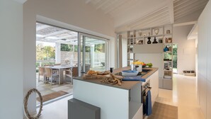 Uma cozinha moderna com uma ilha grande, prateleiras abertas e vista para um pátio externo.
