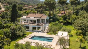 Uma casa moderna de dois andares com piscina, rodeada por vegetação exuberante e colinas.