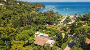 Vista aérea de uma propriedade costeira com piscina, vegetação exuberante e vista para o mar com barcos.