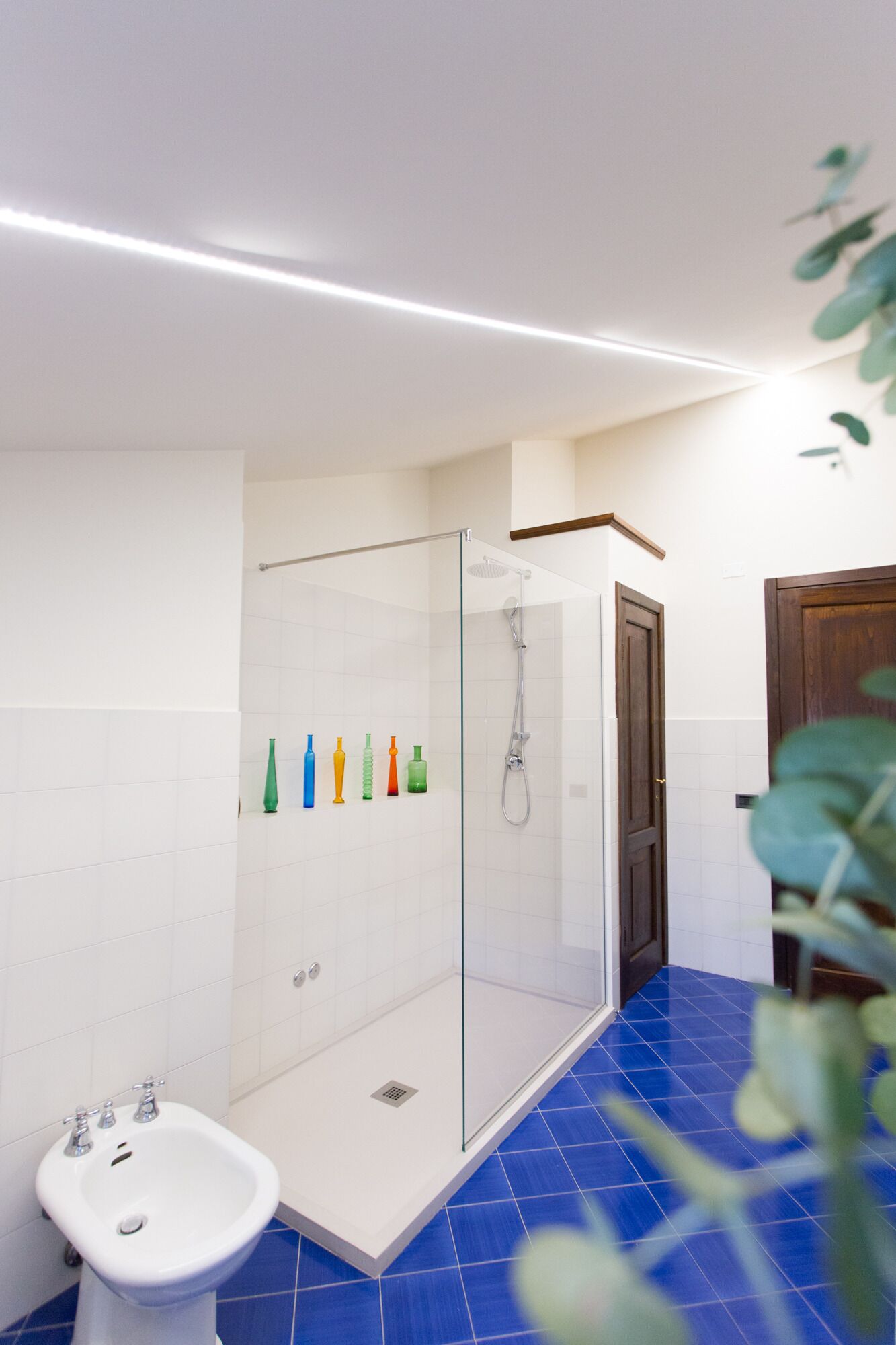 Une salle de bain avec une douche à parois de verre, un lavabo blanc et un sol carrelé de carreaux bleus.