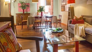 A cozy living room with a wooden ceiling, a dining area with chairs and a table, a sofa with a laptop, and a glass coffee table.