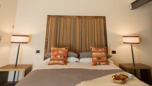 A bedroom with a large bed, two bedside tables, a wooden headboard, and a hanging light fixture.