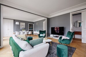 Un soggiorno moderno con un divano grigio, poltrone verdi, una televisione e un'area pranzo sullo sfondo.