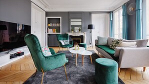Una sala de estar moderna con un sillón verde, un sofá blanco y una mesa de centro. Hay una chimenea, una estantería y un televisor.