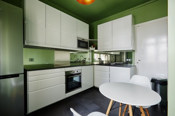 A modern kitchen with white cabinets, a black countertop, and a white dining table. - Emerald Exuberance, by Veeve (Paris)