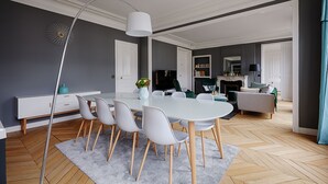 Un salón moderno con una mesa de comedor blanca, paredes grises y un suelo de madera en espiga.