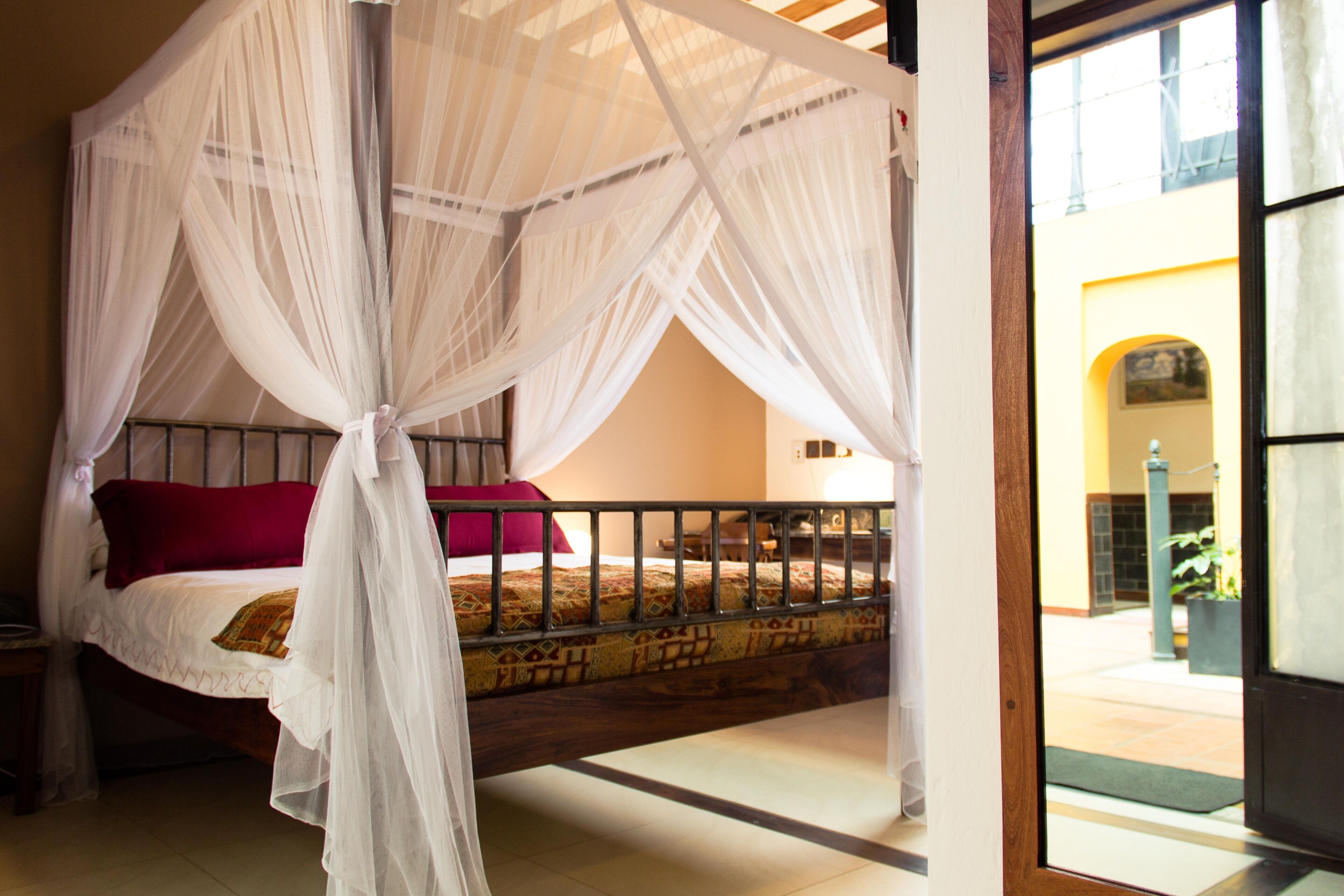 A room with a four-poster bed, a wooden headboard, and a view of the outside through a glass door.