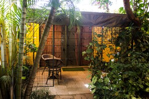 A patio area with a chair, a small table, and a bamboo plant. - Hotel Le Bougainviller (Kampala)