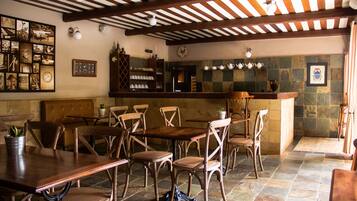 Un restaurante con mesas y sillas de madera, suelo de baldosas y una pared de piedra con un cuadro enmarcado.