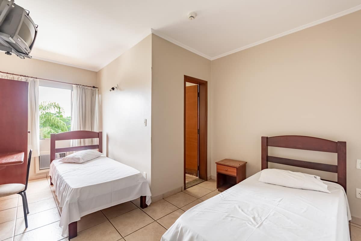 A room with two beds, a chair, a small table, and a television.