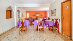 A dining area with multiple tables and chairs, a wooden door, and a tiled floor. - OYO Hotel Vila Rica, Ribeirão Preto (Ribeirão Preto)