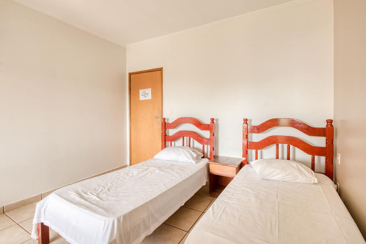 A room with two single beds, wooden headboards, a wooden door, and a tiled floor.