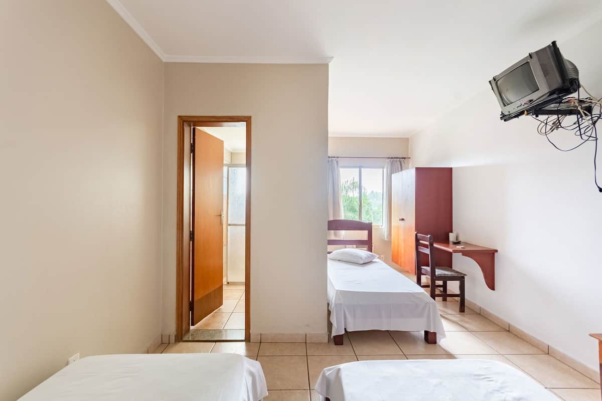 A hotel room with two beds, a desk, a chair, and a television mounted on the wall.