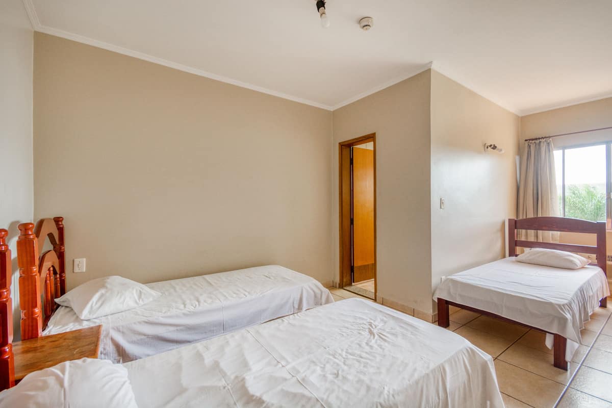 A room with two single beds, a wooden headboard, a wooden bench, and a door leading to another room.