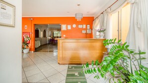 A reception area with a wooden desk, a green patterned rug, and potted plants. - OYO Hotel Vila Rica, Ribeirão Preto (Ribeirão Preto)