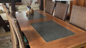 Een eetruimte met een lange houten tafel, rieten stoelen en hangende witte吊り下げ型照明.