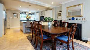 Un'area pranzo con un tavolo e sedie in legno, un tappeto blu con motivi decorativi e un caminetto sormontato da uno specchio.