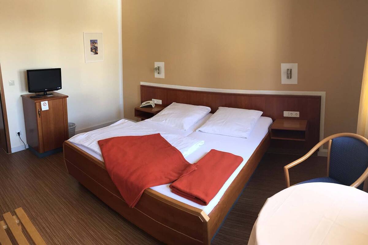 Una habitació d'hotel amb un llit gran, una televisió sobre una estanteria, un escriptori i una cadira.