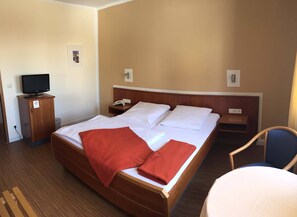 A hotel room with a large bed, a television on a cabinet, a desk, and a chair.