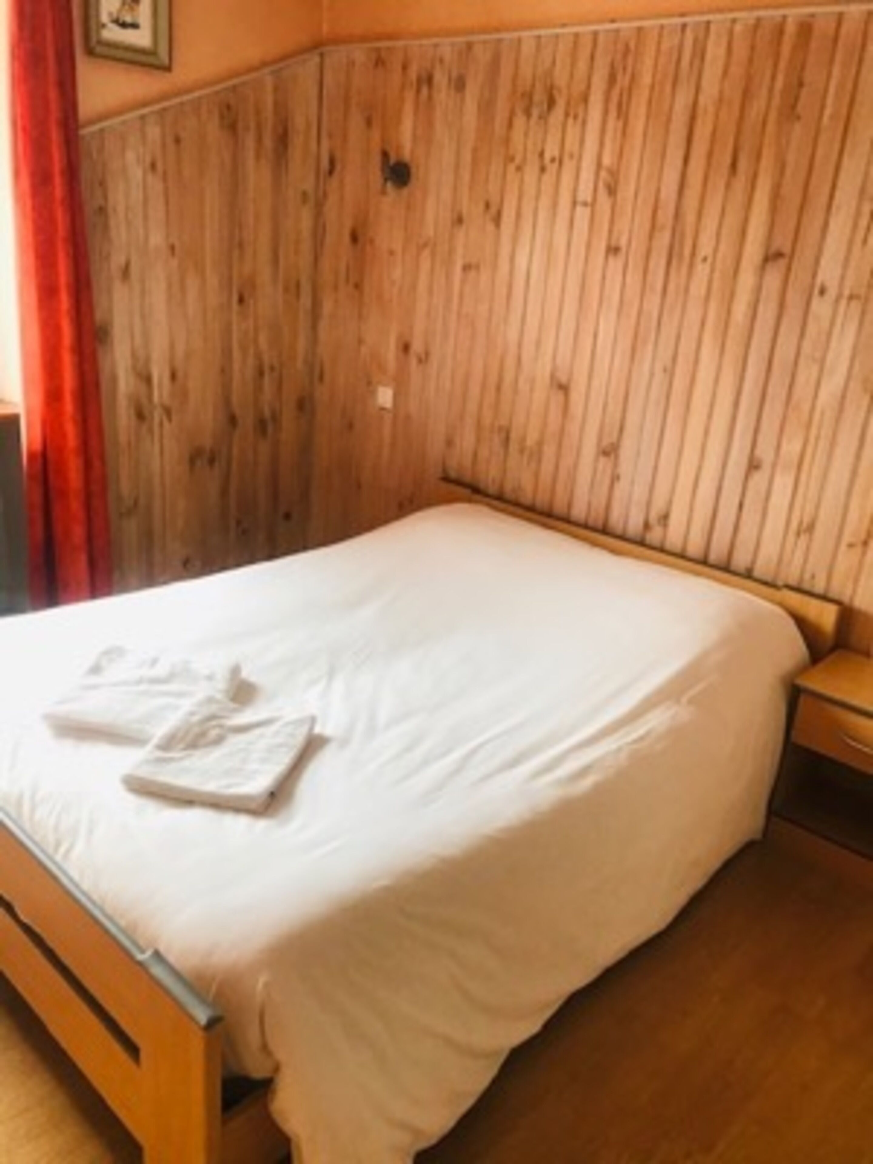 A bedroom with a wooden headboard, a bed with white bedding, and a nightstand with a lamp.
