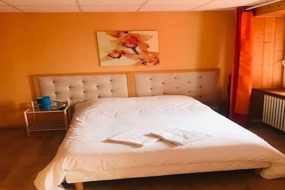 A hotel room with a large bed, a headboard, a bedside table with a lamp, and a painting on the wall.