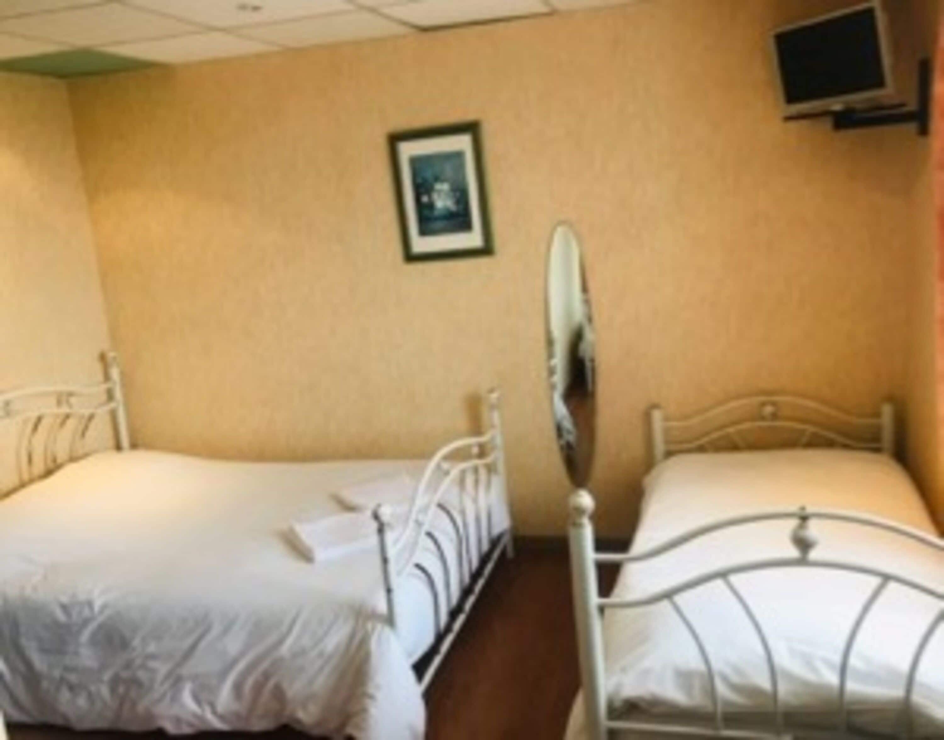 A room with two single beds, a small mirror, and a television on the wall.