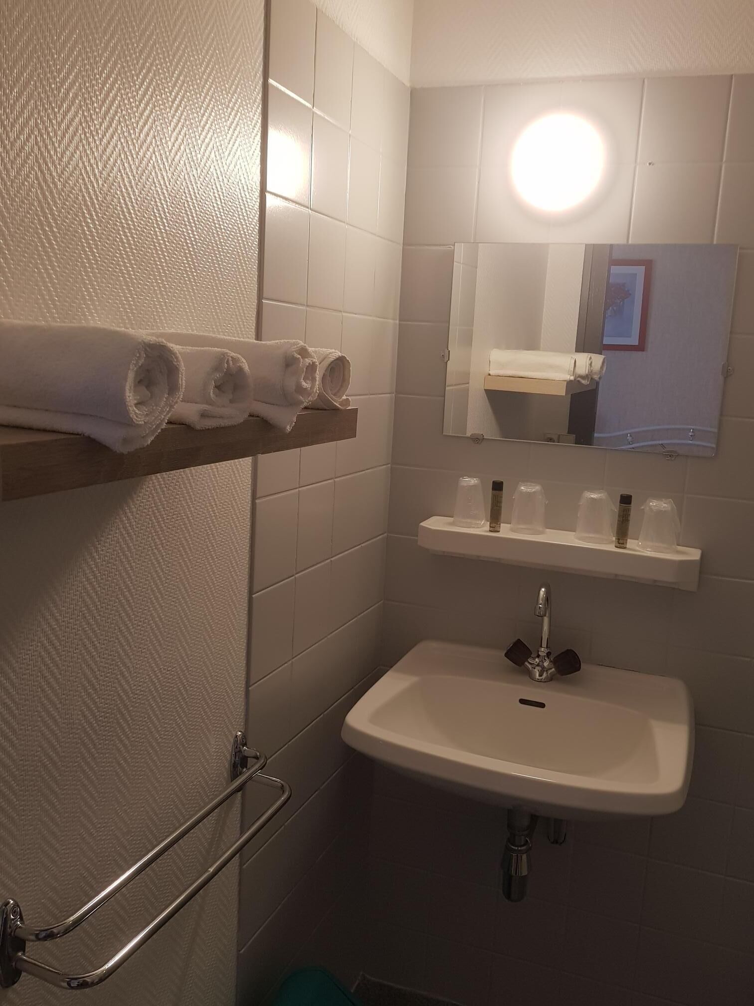 Un baño con un lavamanos blanco, un espejo y un perchero con toallas enrolladas.