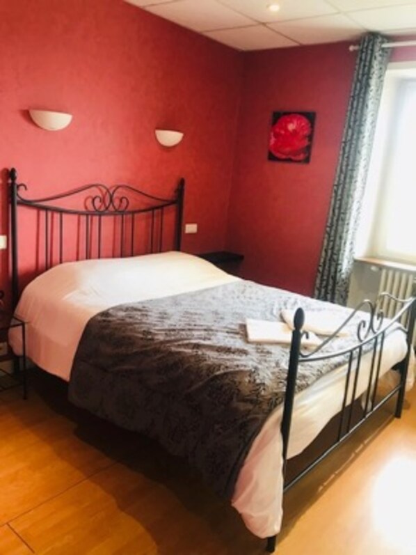 A bedroom with a metal bed frame, a white bedspread, and a dark throw blanket. - Hotel des Cevennes (Mezilhac)