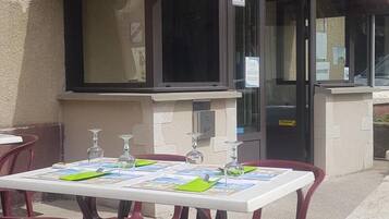 Um restaurante com mesas ao ar livre, telhado de azulejos e venezianas vermelhas.