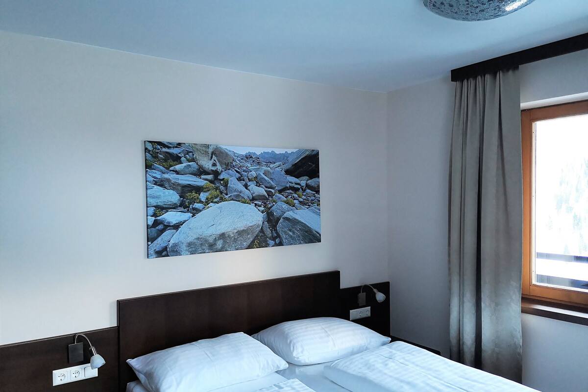 A hotel room with a bed, a wall-mounted lamp, and a painting of a rocky landscape.