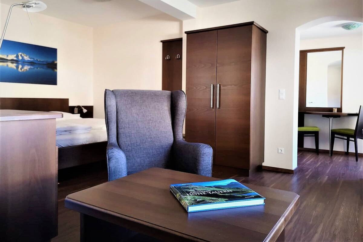 A hotel room with a bed, a desk, a chair, a wardrobe, and a book on the desk.