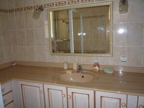 A bathroom with a beige sink, a mirror with a decorative frame, and a shower area.