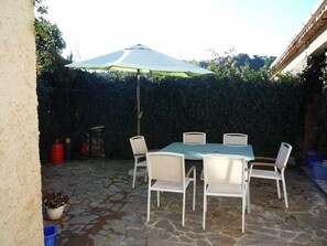 An outdoor patio with a stone floor, a table with chairs, and a white umbrella.