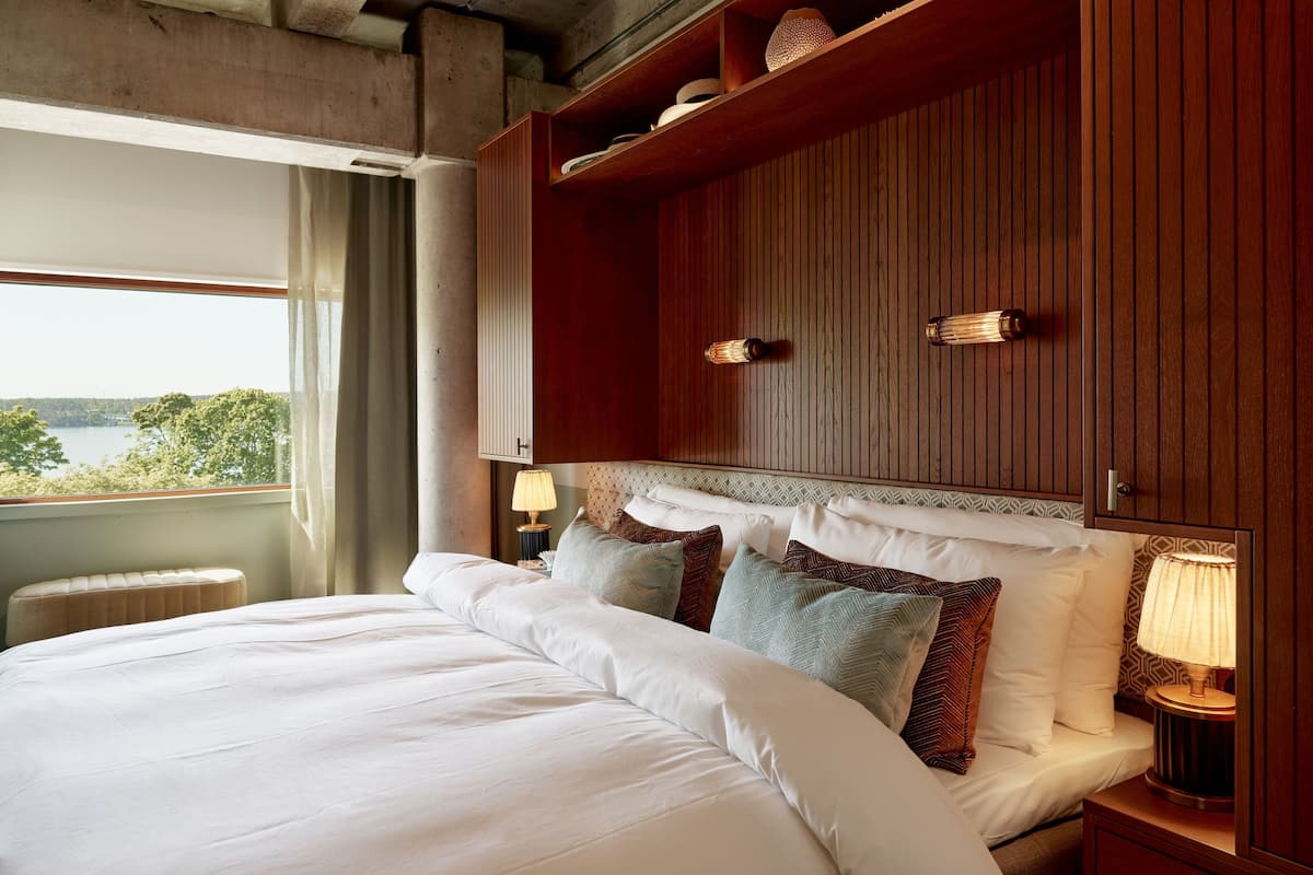 Une chambre d’hôtel avec un grand lit, une tête de lit en bois, une table de chevet avec une lampe et une vue sur un lac.