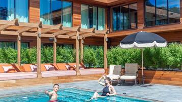 A modern outdoor pool area with wooden pergolas, lounge seating, and a large umbrella.