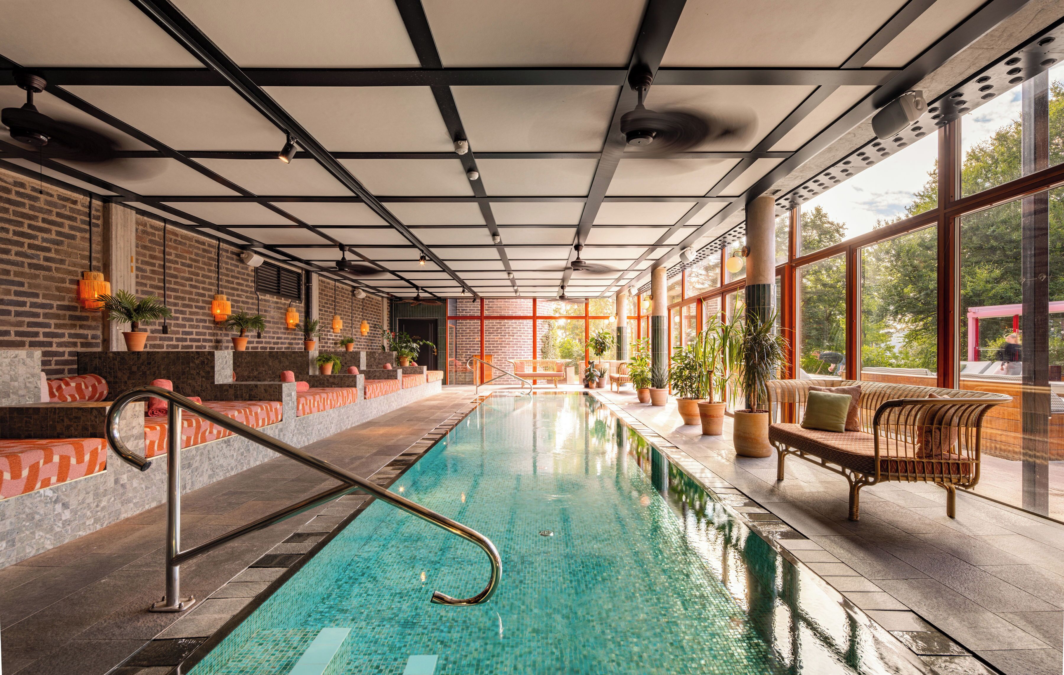 Una piscina interior con vistas despejadas al cielo a través de amplios ventanales, rodeada de asientos y plantas en macetas.