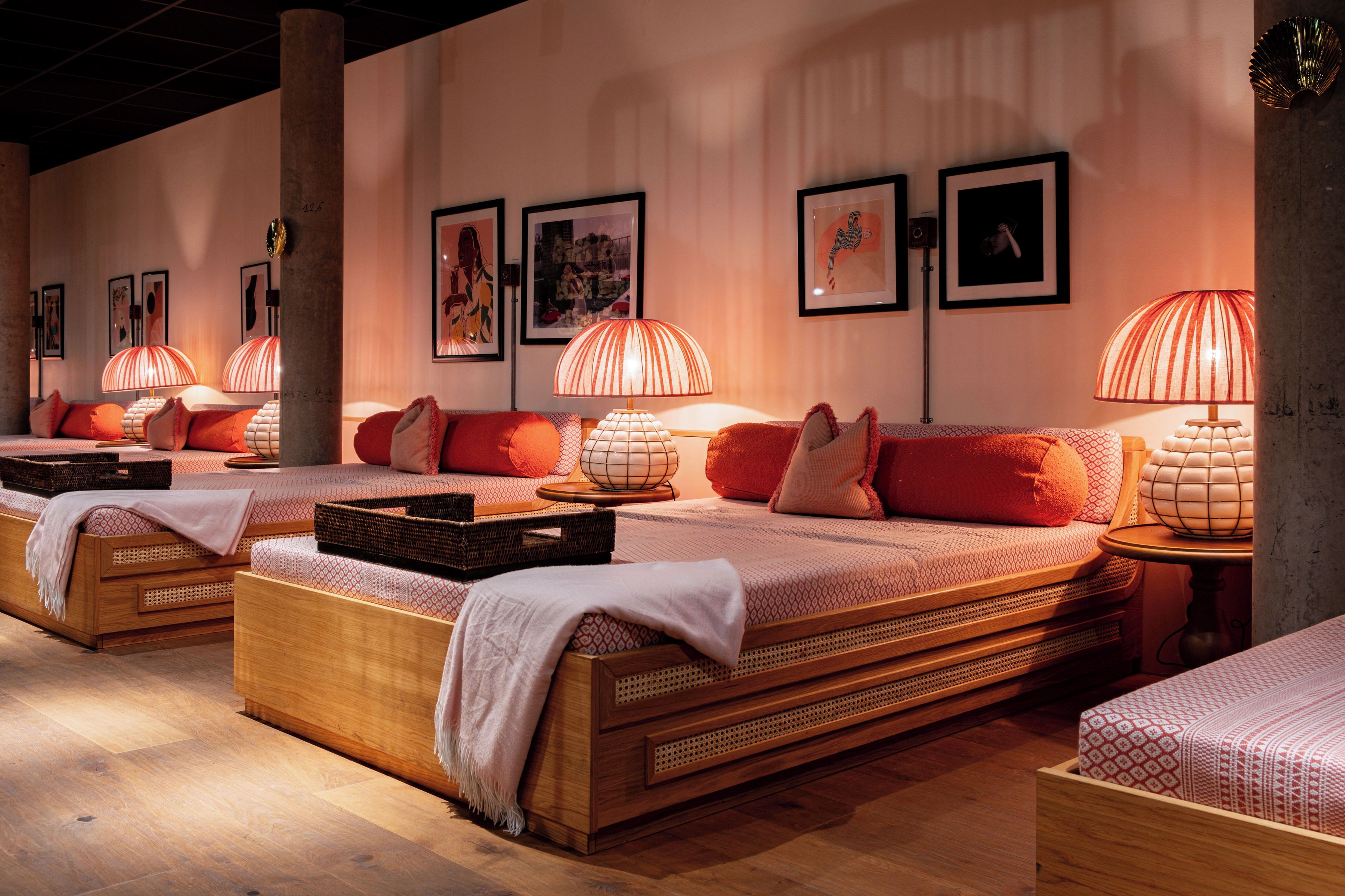 Une chambre d’hôtel dotée de plusieurs lits, chacun ayant une tête de lit au design unique, et d’une grande fenêtre laissant entrer la lumière naturelle.