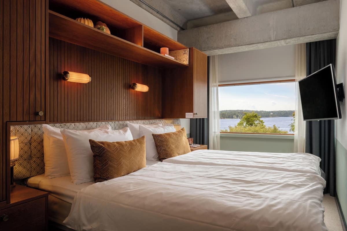 Une chambre d’hôtel avec un grand lit, une tête de lit en bois, des étagères intégrées et un téléviseur fixé au mur.