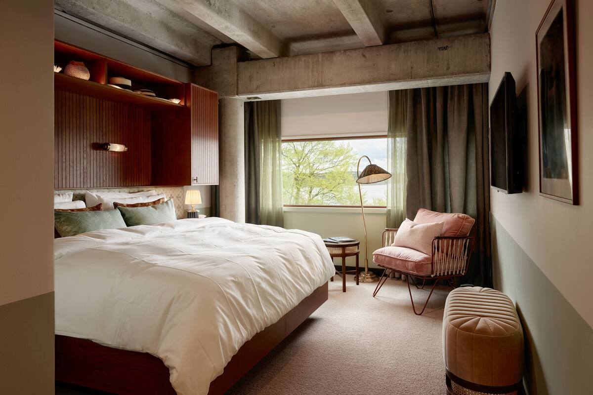 Une chambre à coucher avec un grand lit, une chaise, une petite table et une lampe sur pied.